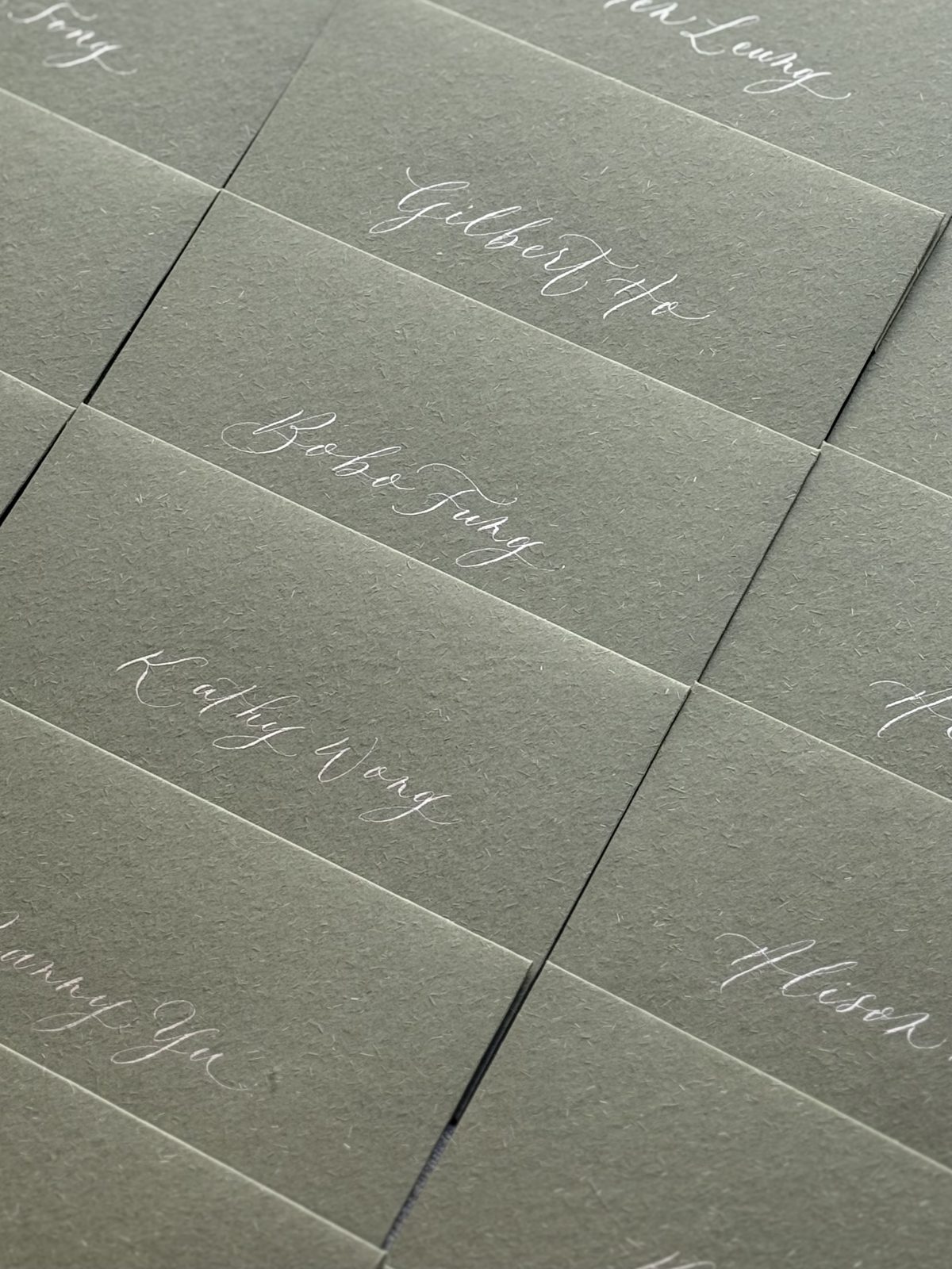Sage green envelopes addressed in white calligraphy for an event invitation mailing
