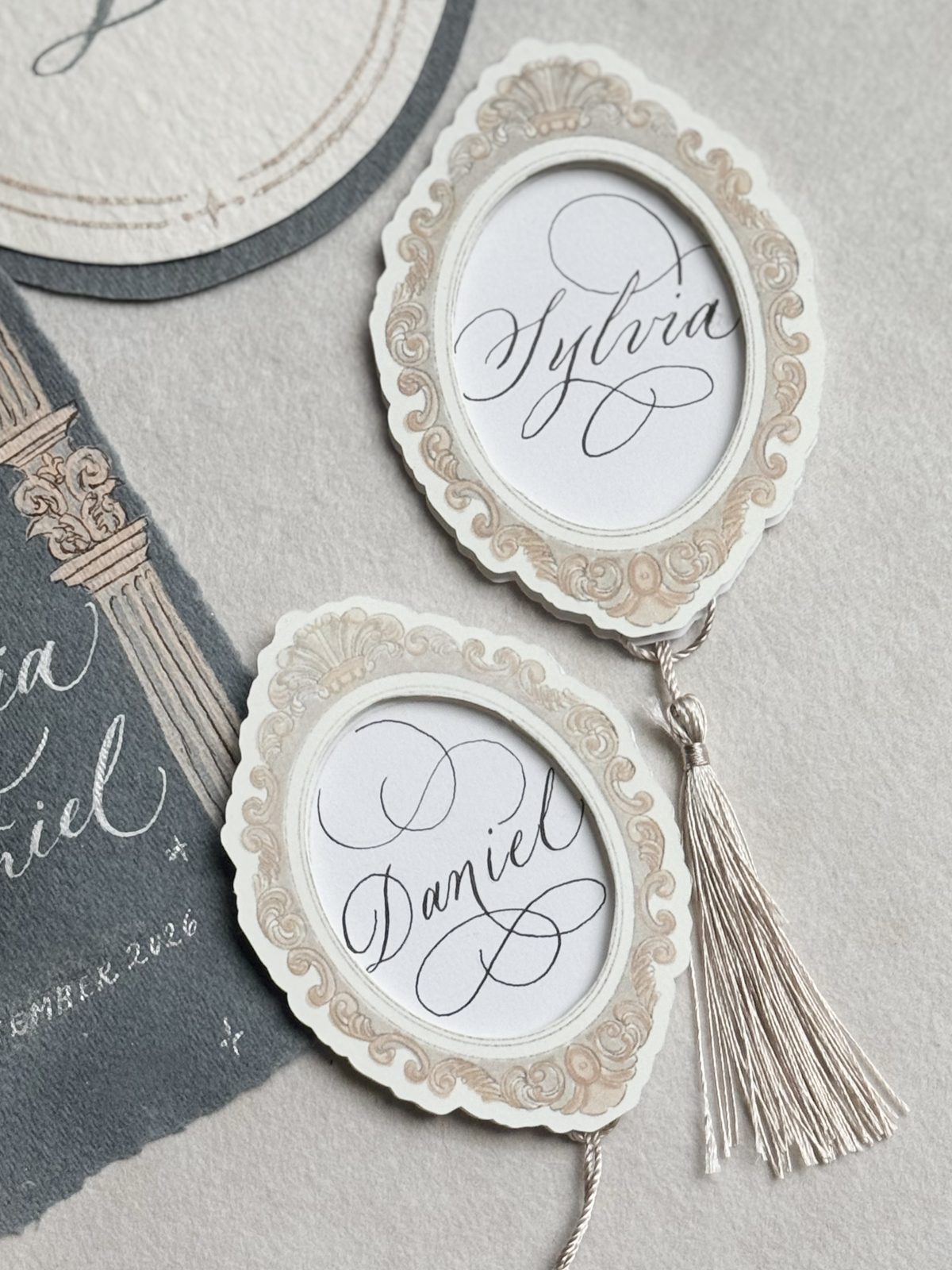 Oval place cards with guest names in white calligraphy and silk tassels