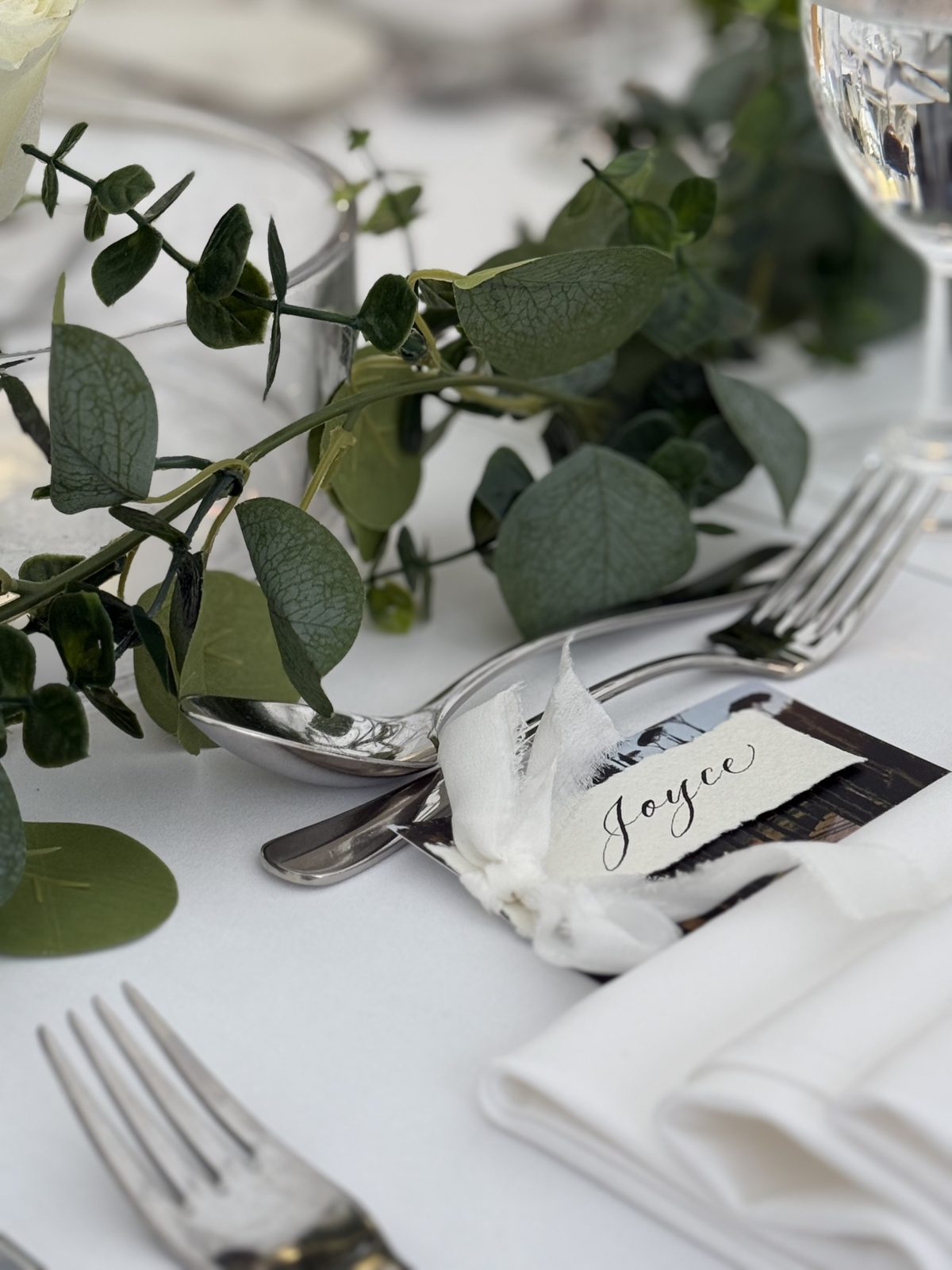 Calligraphed place card set on a napkin with eucalyptus at a wedding table setting