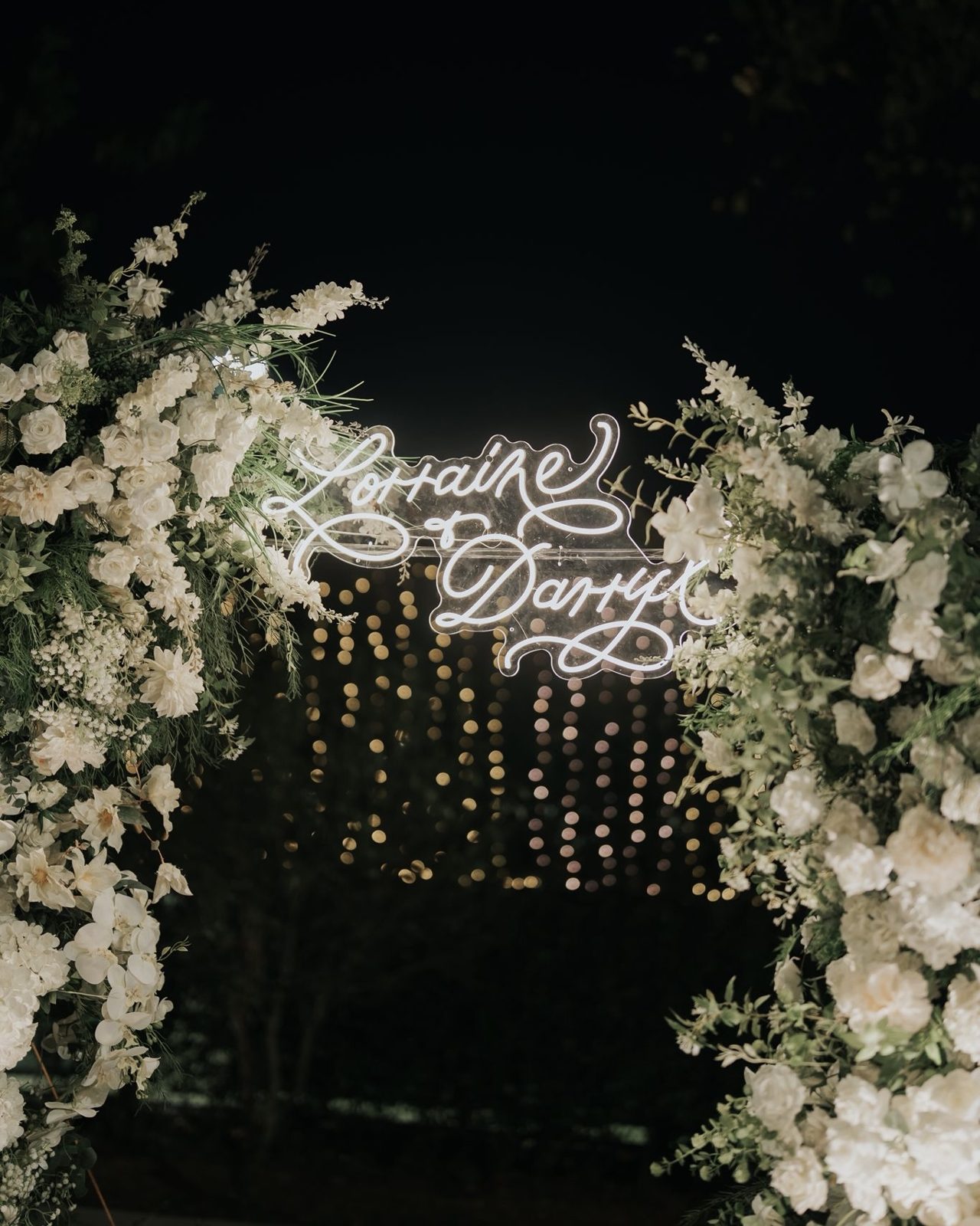 Wedding stage backdrop with calligraphed names in lights and hanging greenery