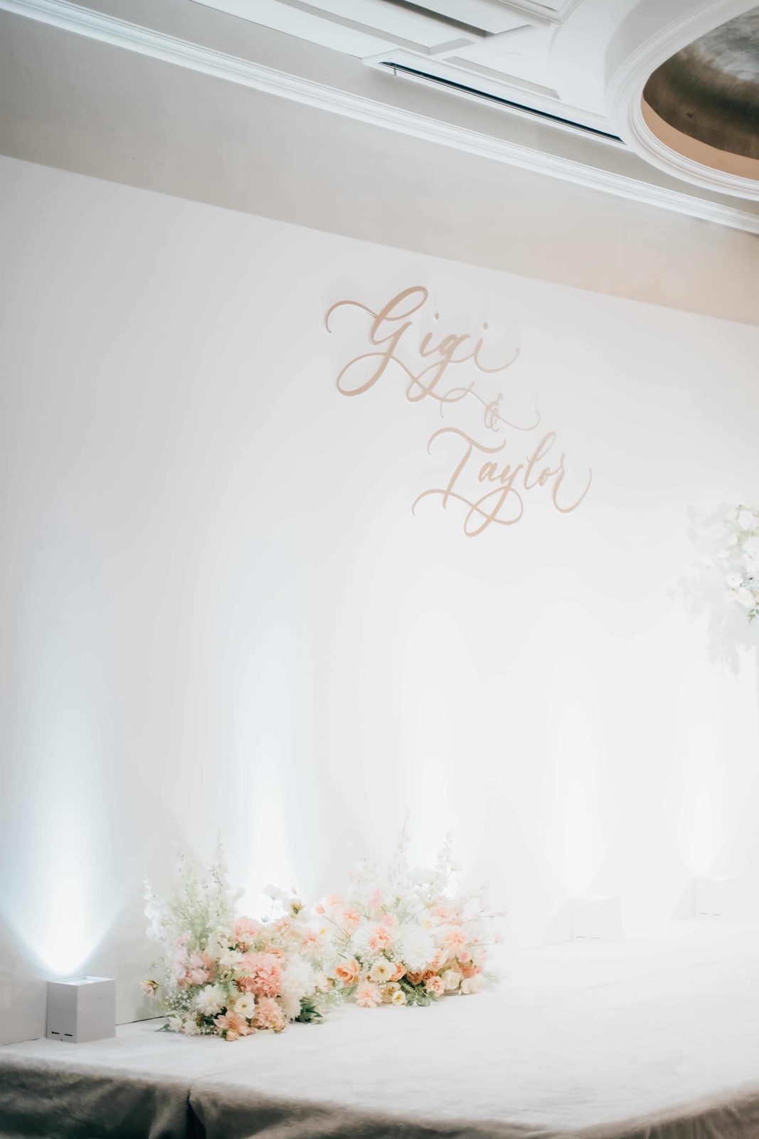 Minimal white wedding backdrop with calligraphed couple monogram and floral base